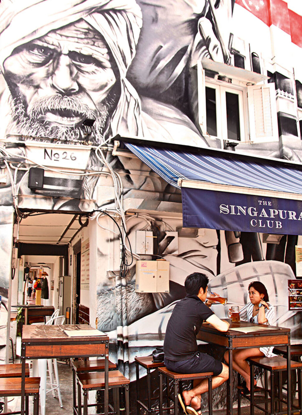 Two people sitting at a café. A mural of a man with a beard wearing a turban is above them.