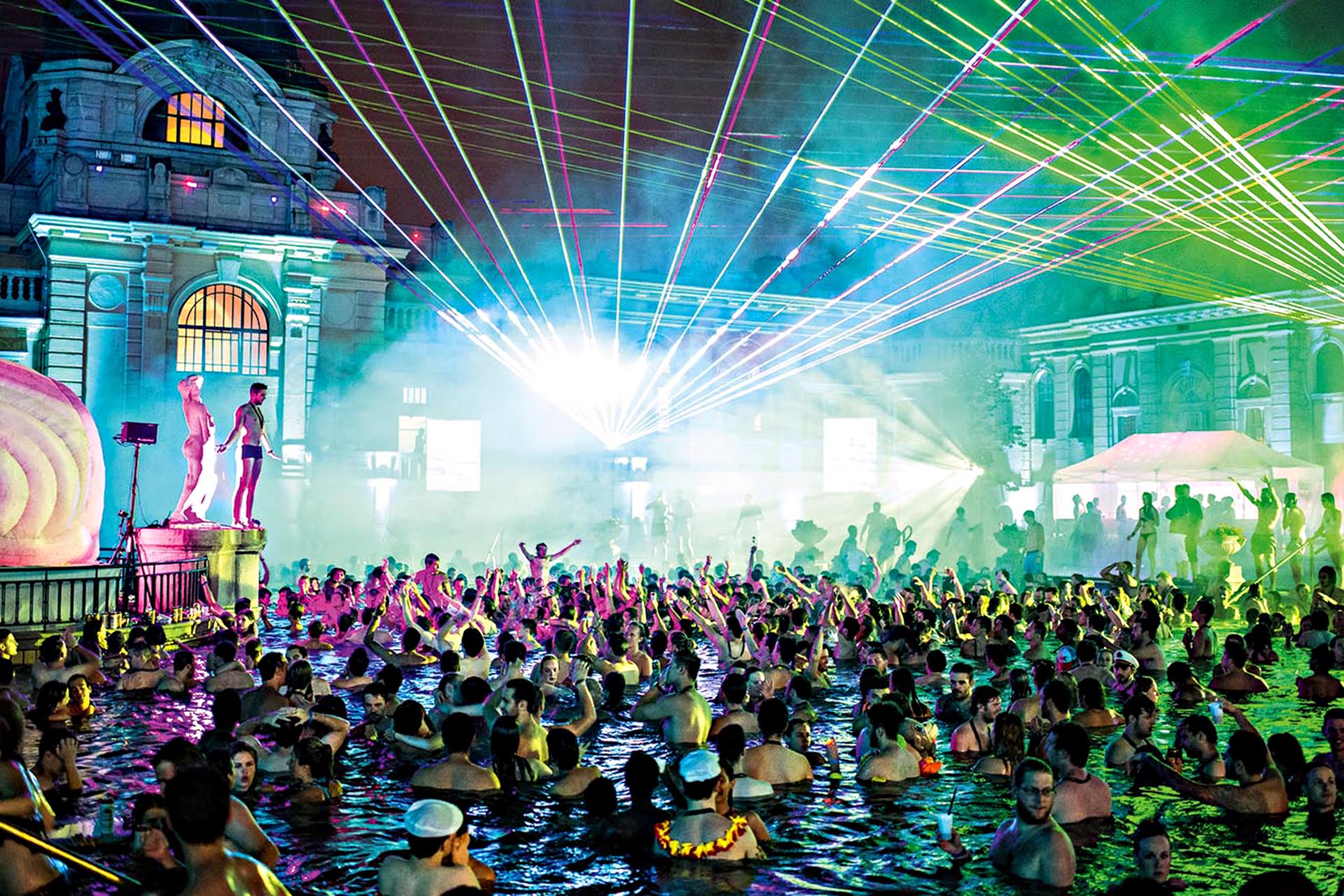 A huge rave in a pool with lasers everywhere. It is packed with people in their bathers.
