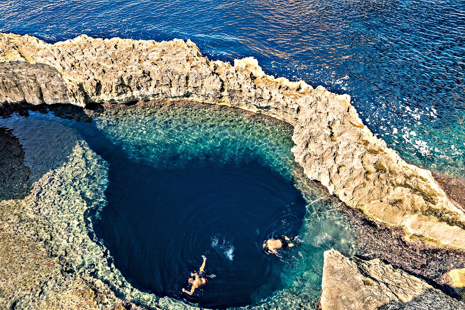 Two people swimming in an enclosed rock pool.