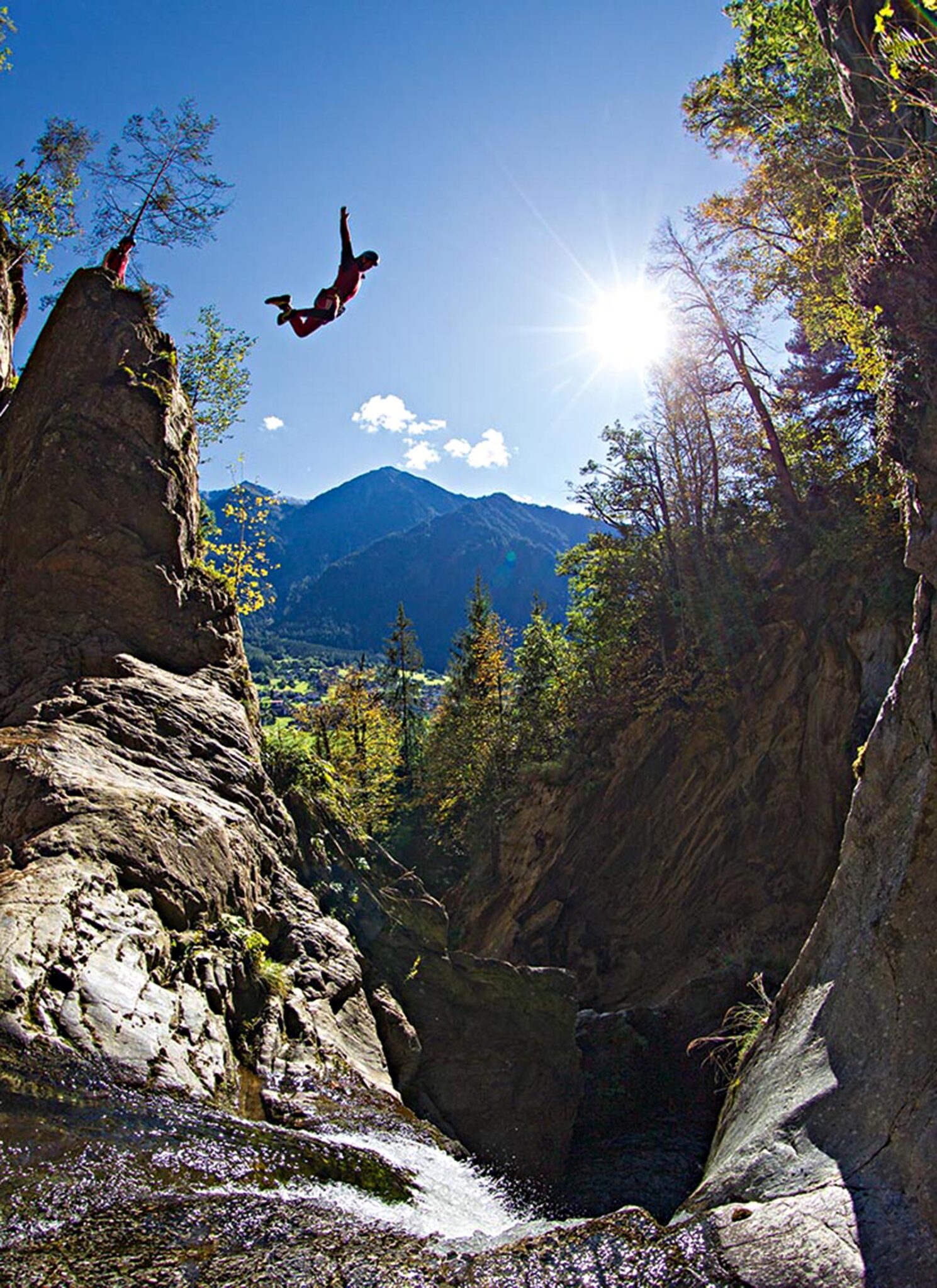Somebody jumping into a canyon of rushing water from a very high rock.