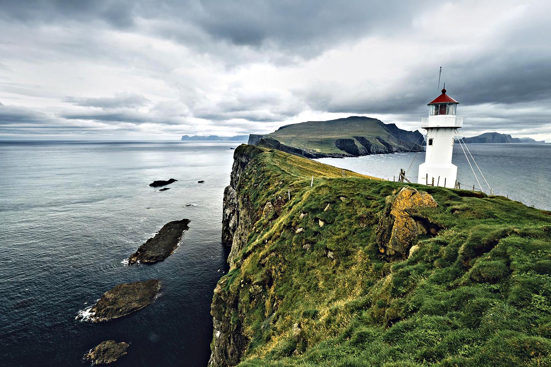 A white lighthouse on a high mountain with a steep drop to the sea.