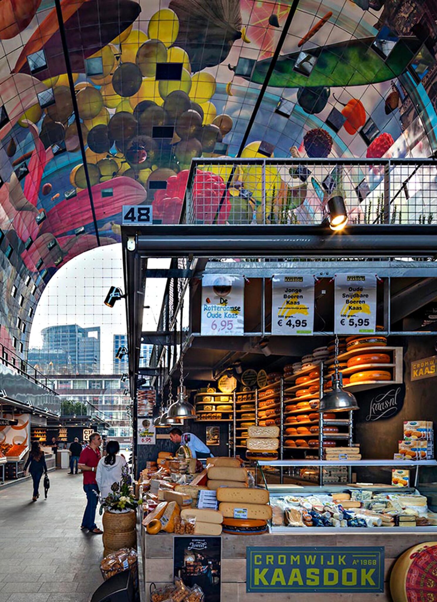 A gourmet cheese shop in the market, with a man working the counter in a blue uniform.
