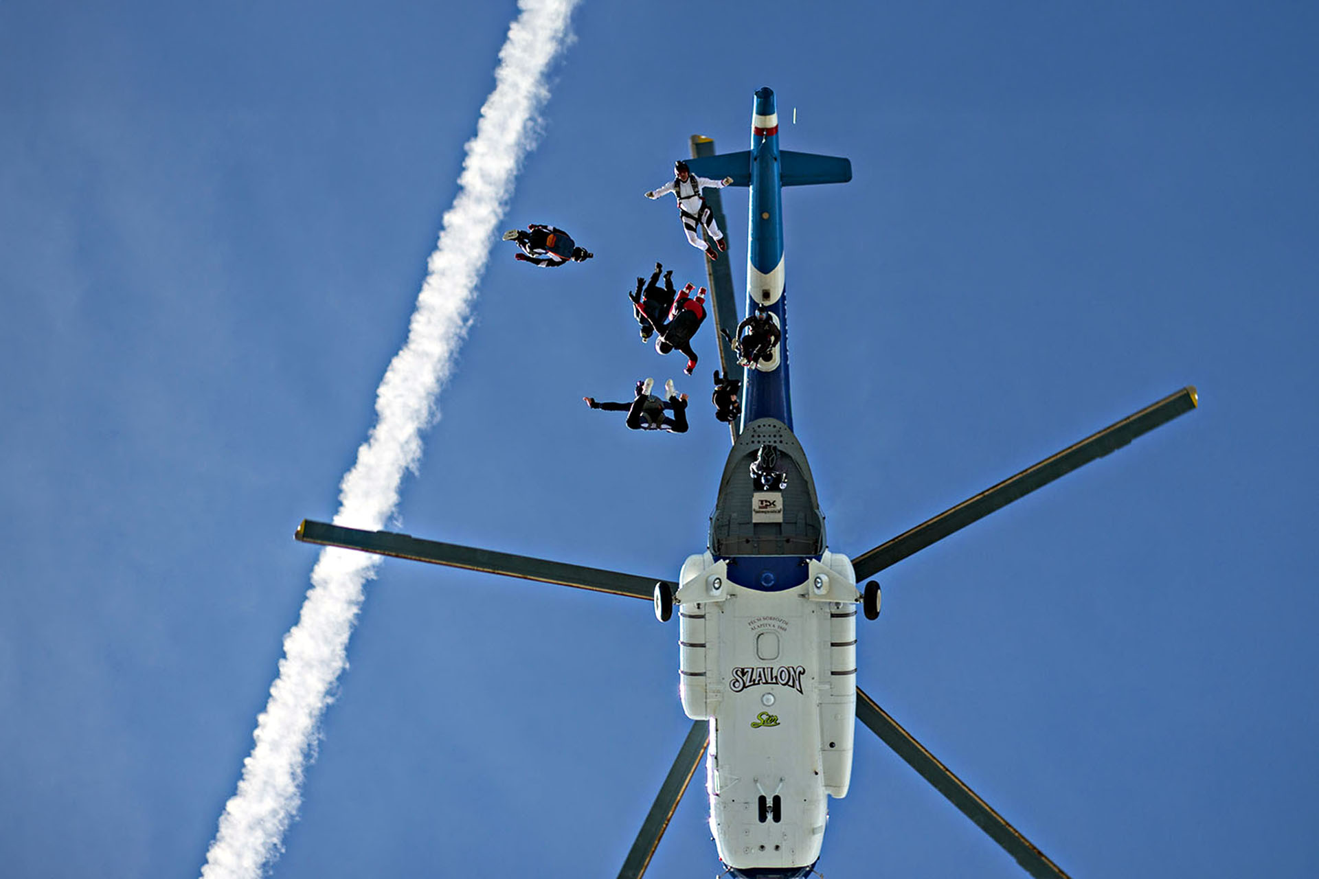 A low angle of five people sky diving out of a helicopter.