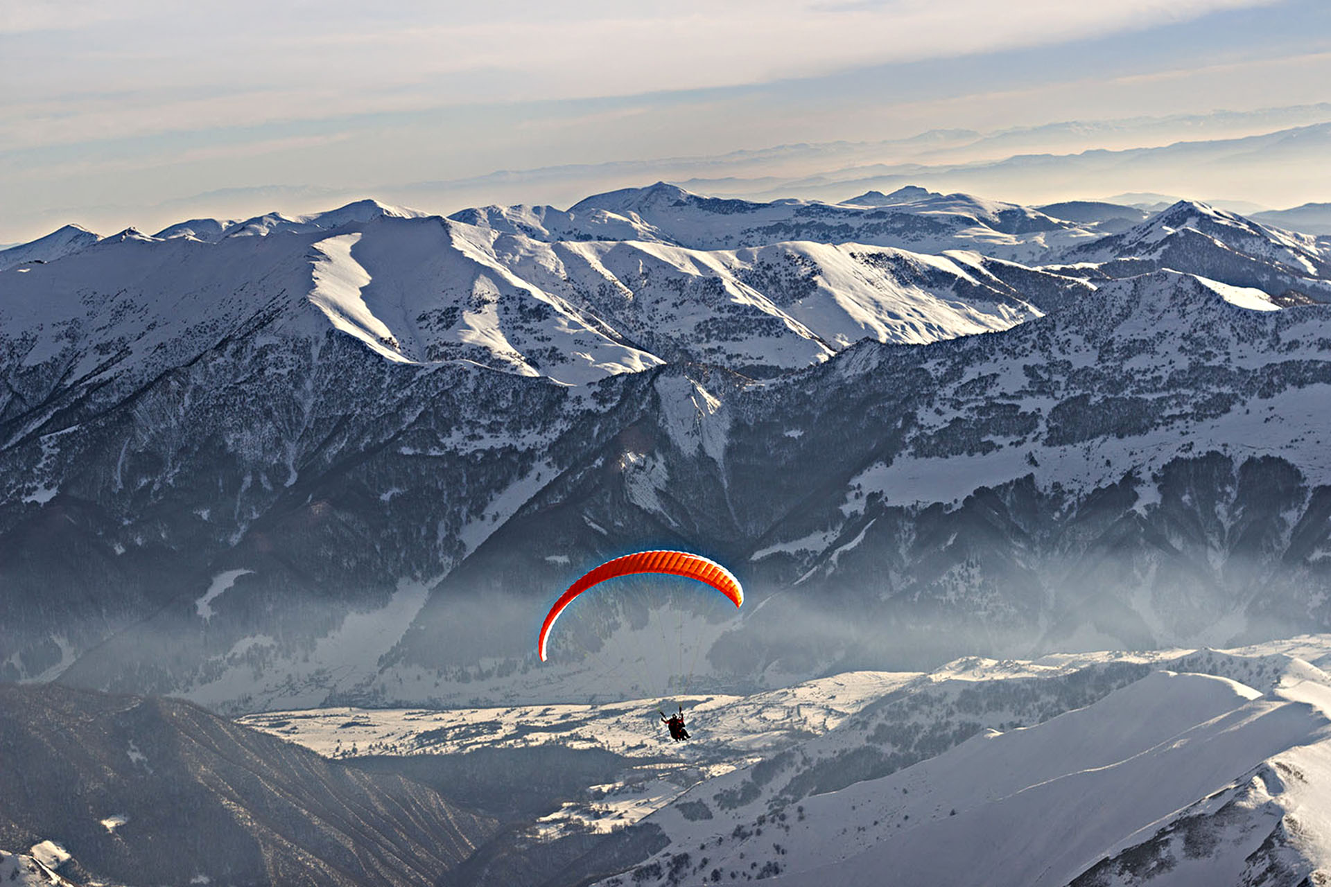 A person parachuting through snowy mountain ranges.