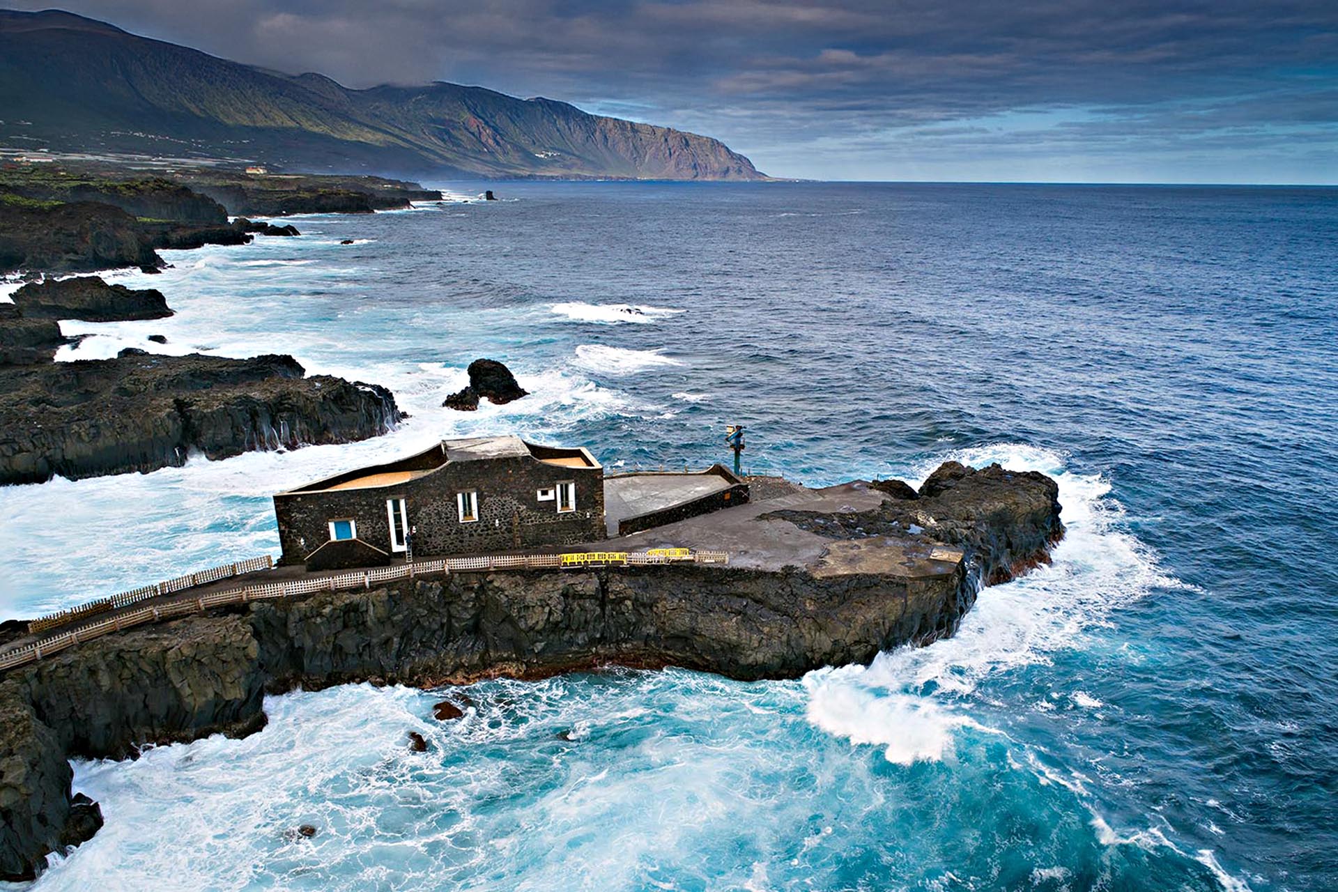 A house on a very narrow strip of rock in the middle of the water.