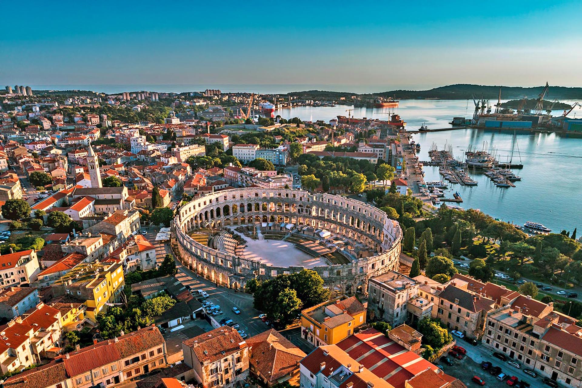 An aerial shot of an old city on the water. In the middle, a circular coliseum.