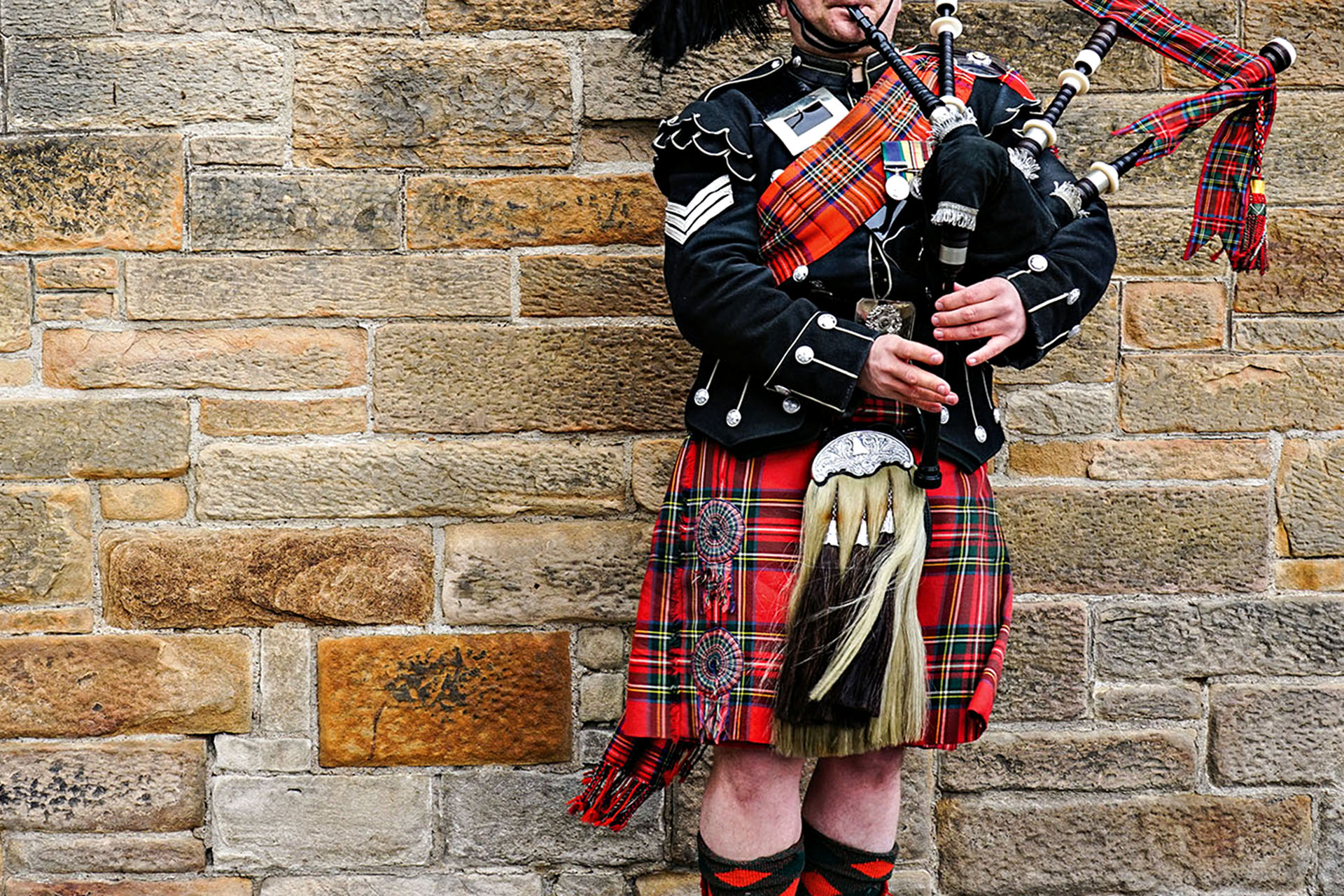 A person in traditional Scottish-wear playing the bagpipes.