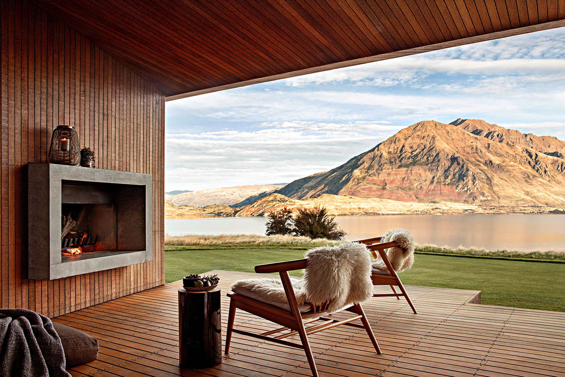 Two chairs and a fireplace on an outside deck, with a view of mountains.