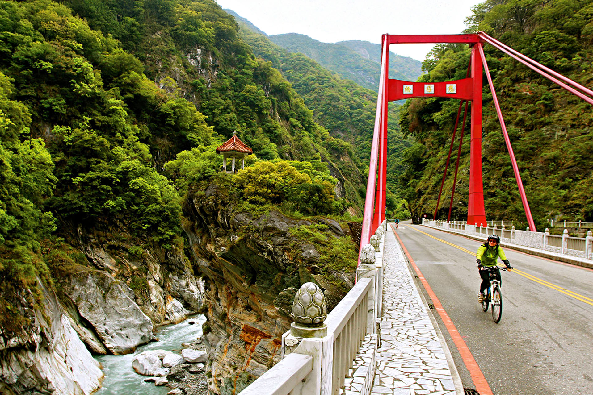 A person on a bike riding over a bridge with red decorations.