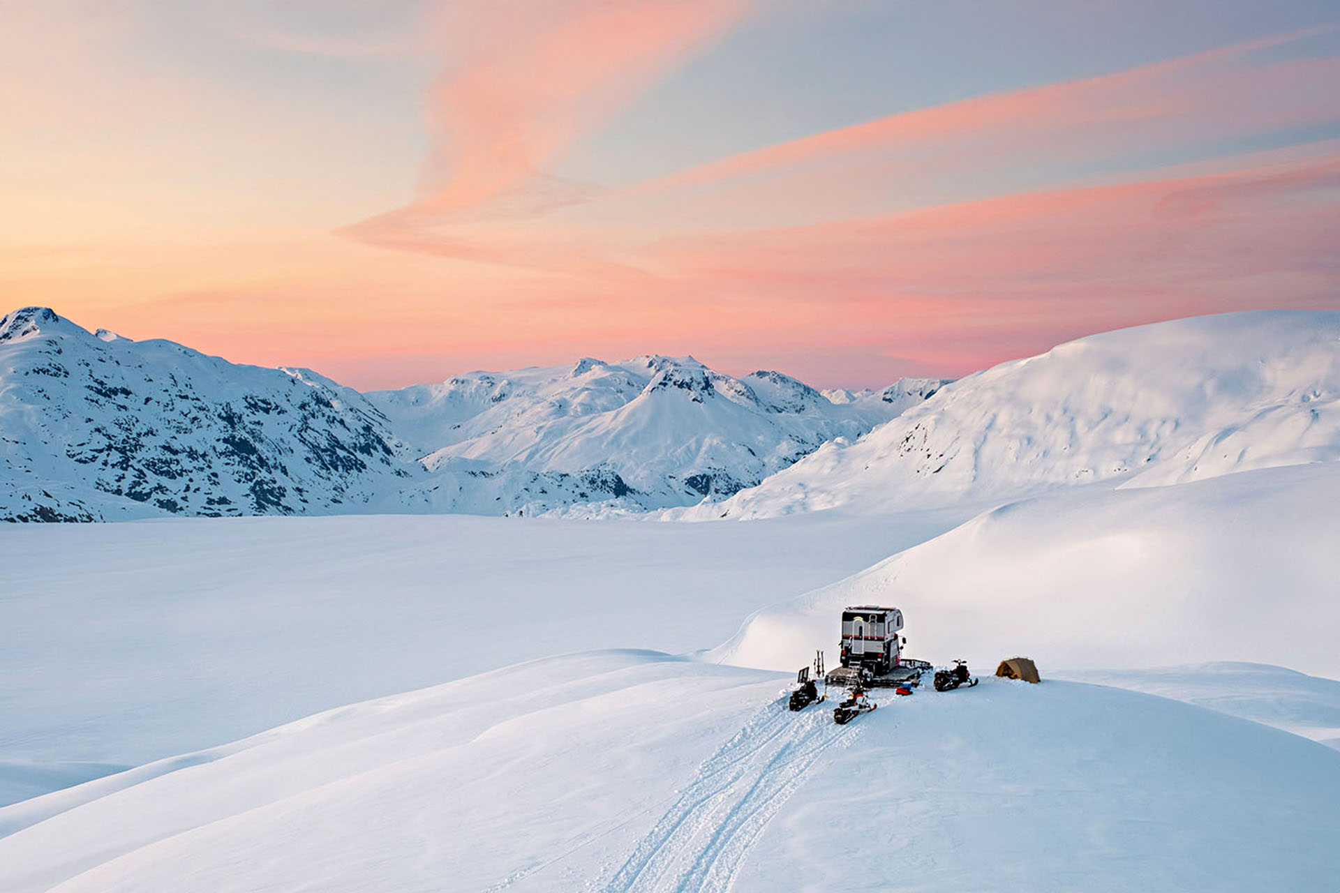 A snowcat camper being driven through the snowy hills.