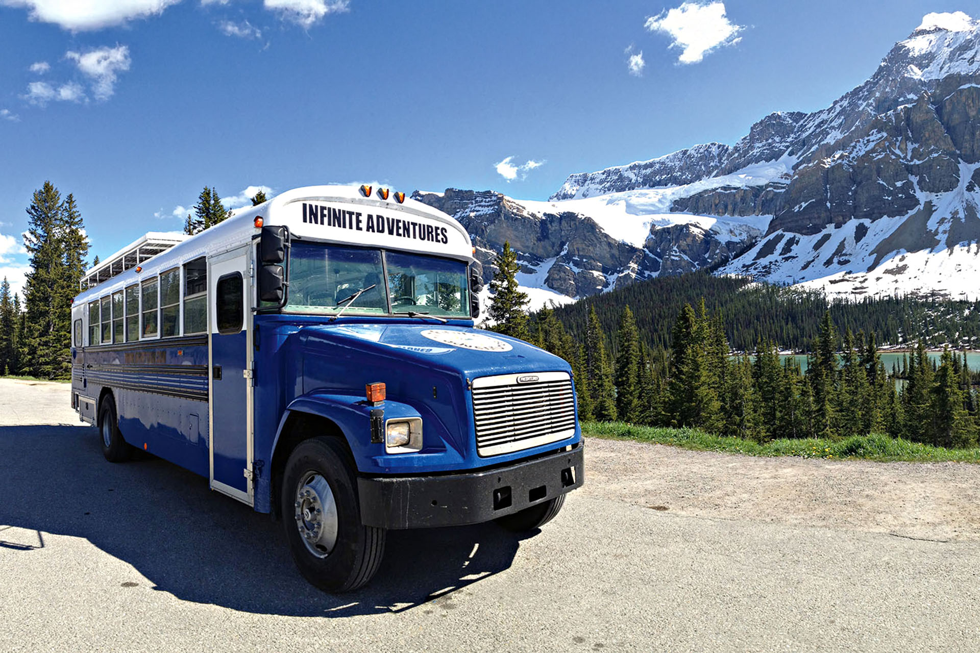 A blue bus next to the snowy mountains.