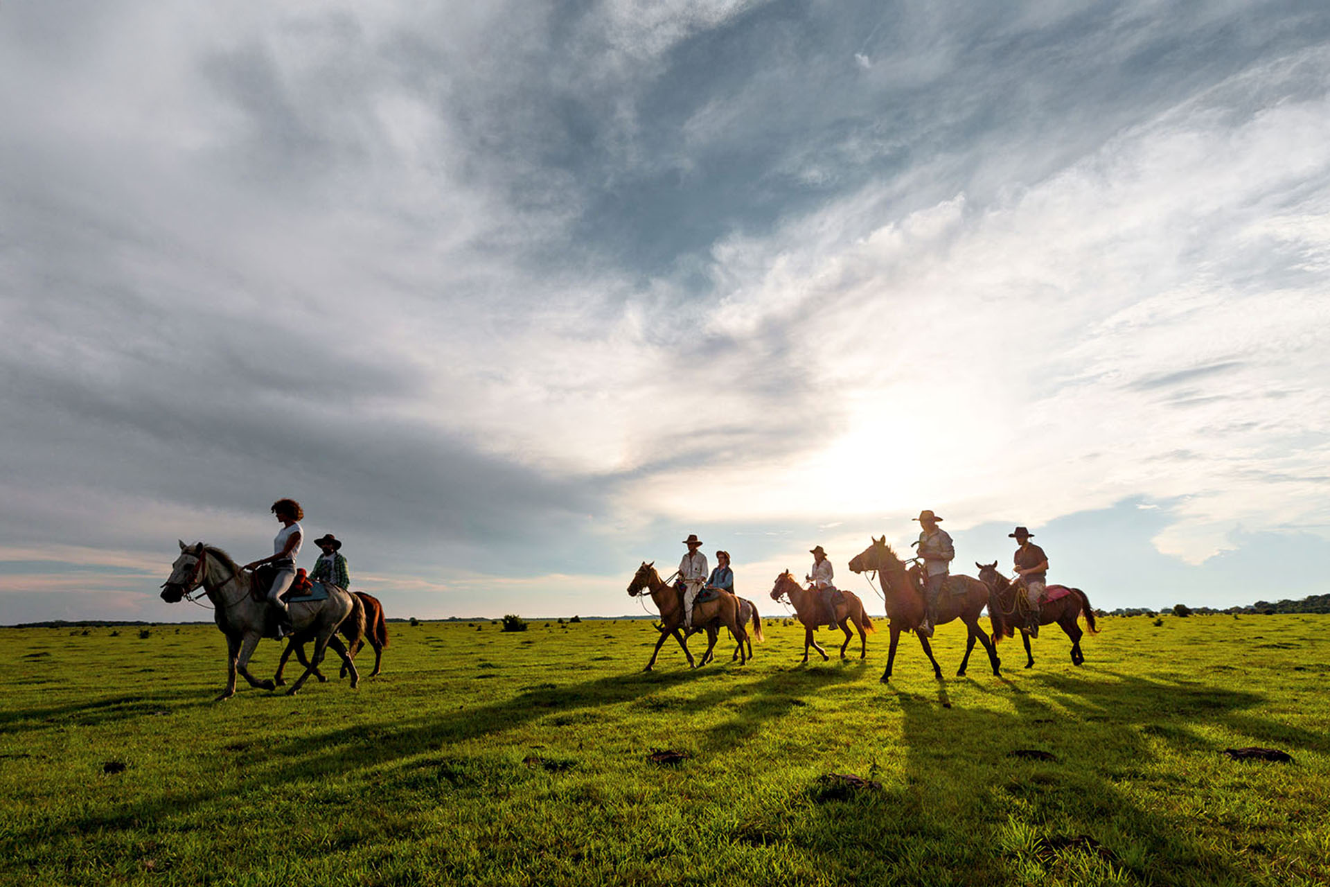 Six people on horseback riding through a field.