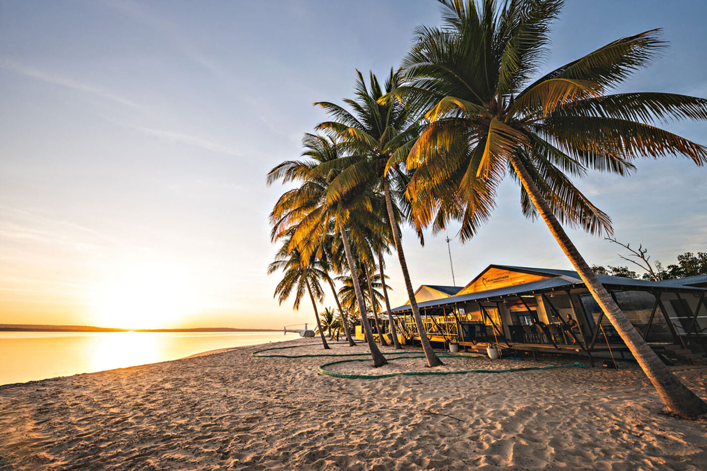 A sunset over a beach filled with palm trees and little shacks.