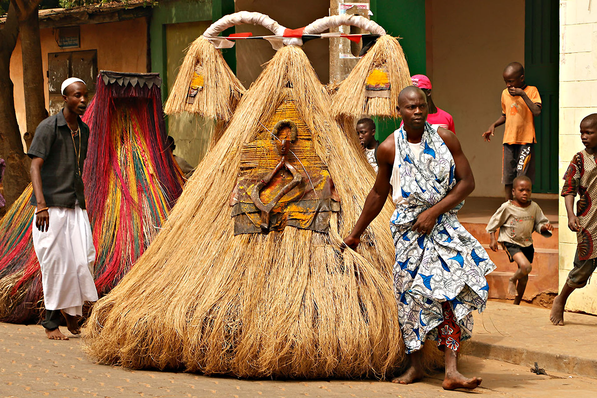 A person in a big straw skirt that covers their entire body, being lead by a man through the street.