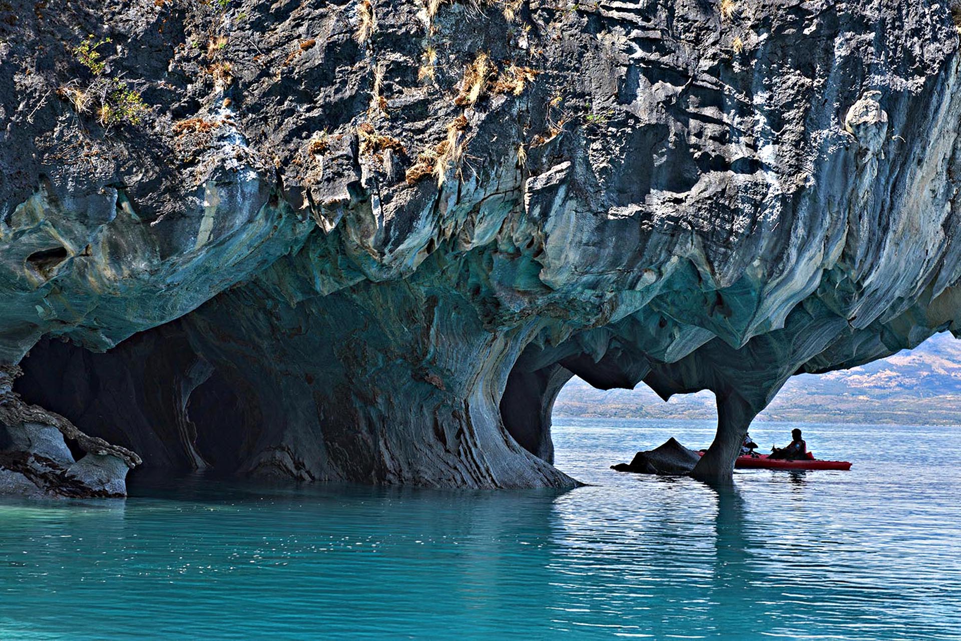 A cave formation over the water, a person in a boat is floating underneath it.