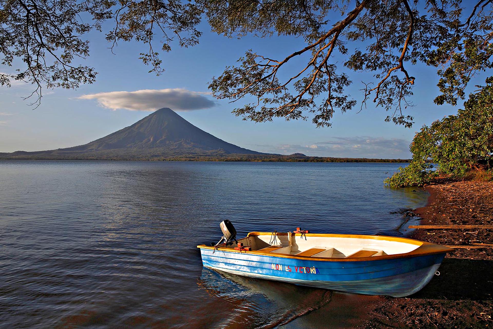 A boat parked half on land, in the background, a big volcano.
