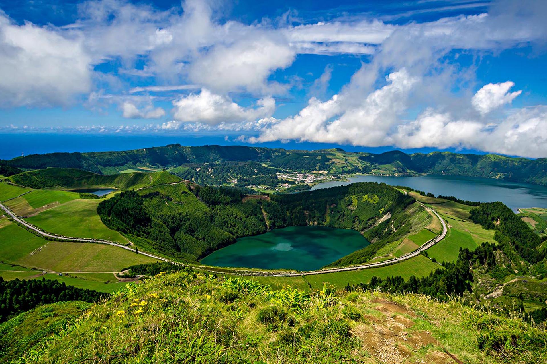 An aerial shot of a small lake in a basin formation, with greenery slanted all around it. Behind it, another big lake.