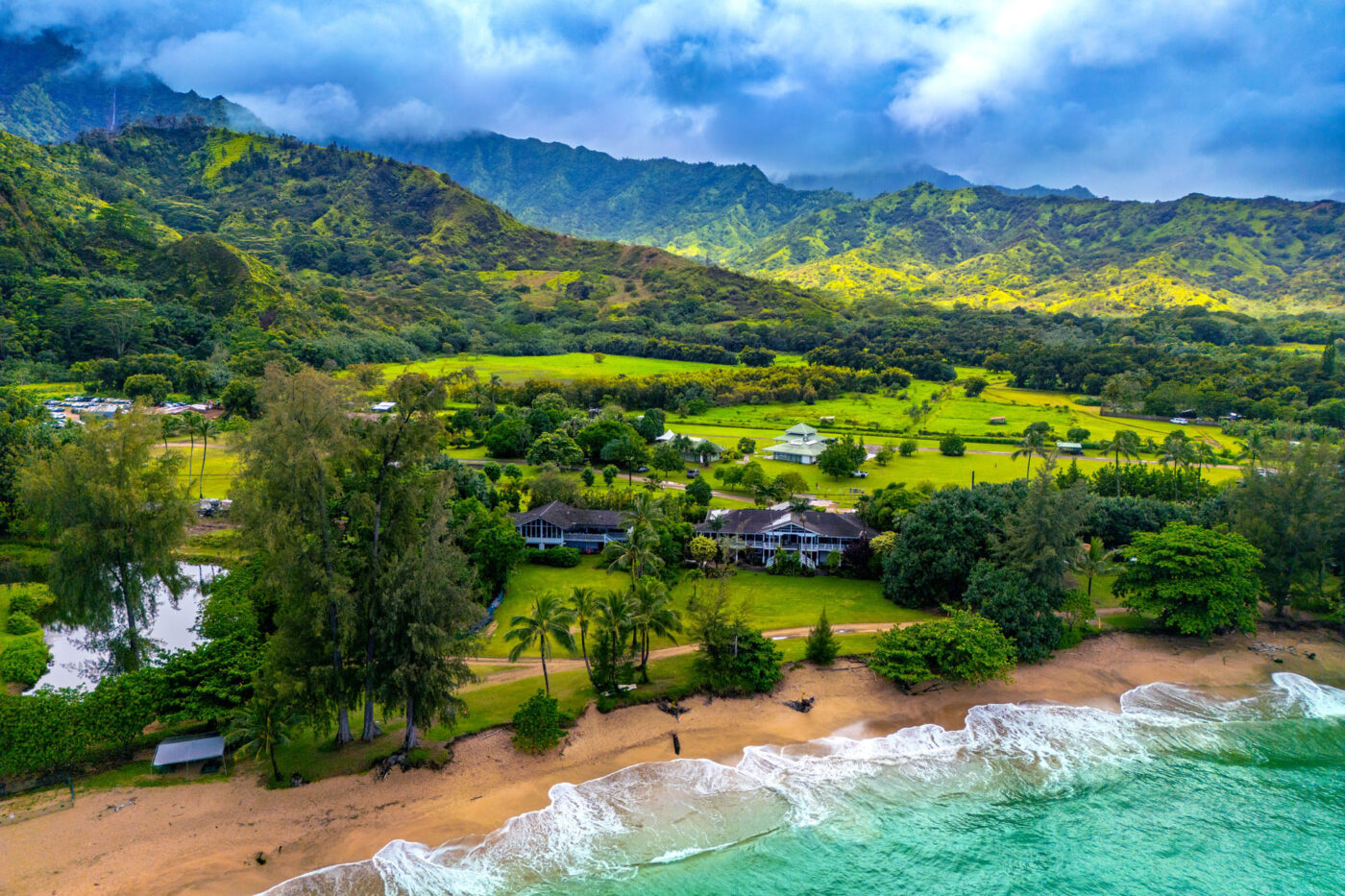 A landcape shot of some big houses by the sea. Mountains tower behind them.