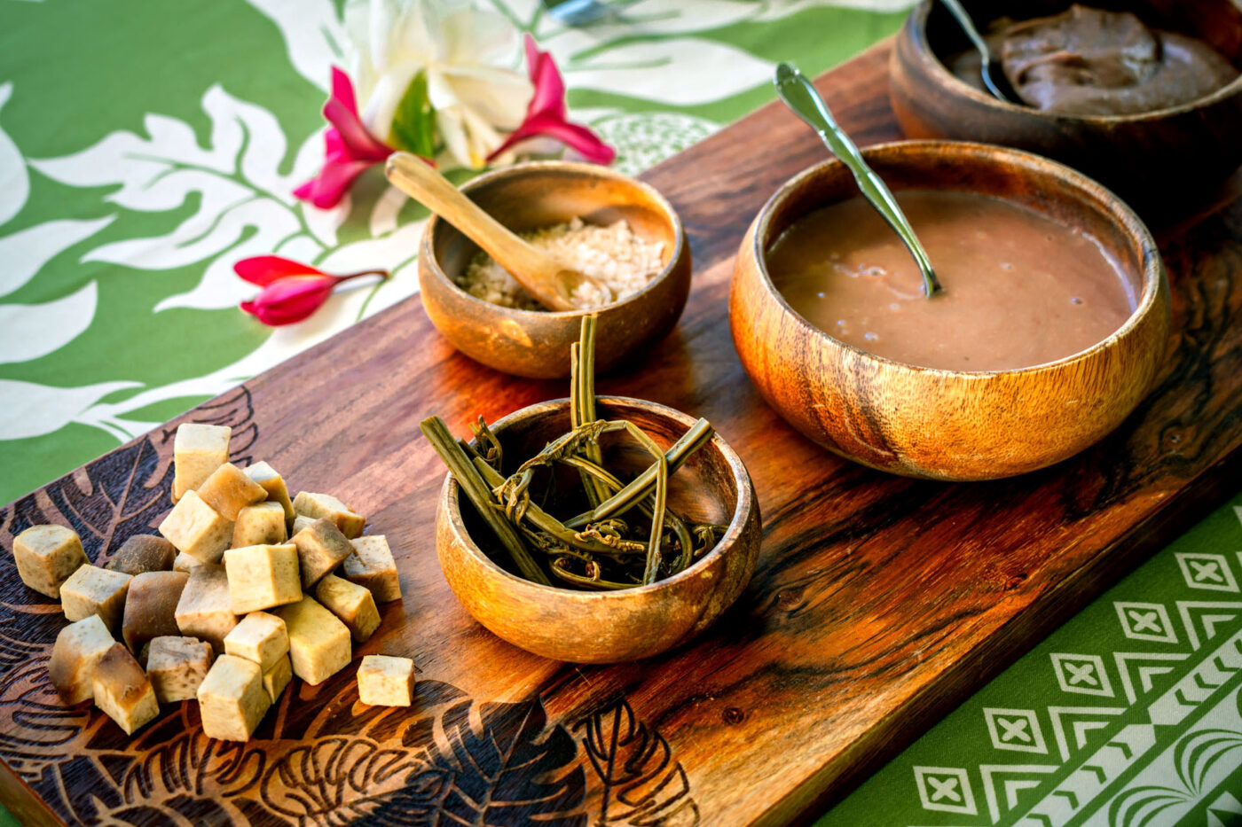 Bowls with different soups, broths and vegetables laid out on a wooden board.