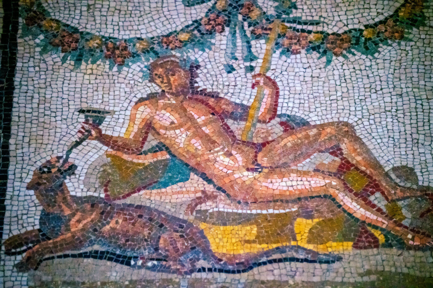 Mosaic art of a naked person lying on something and holding a funnel into an animal's mouth.