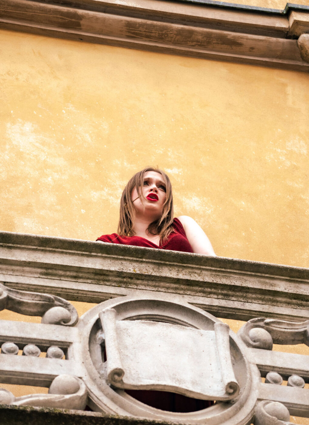 A woman singing opera in a red dress on a balcony.