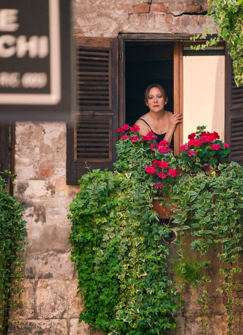 A woman singing through a window with flowers all around it.